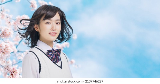 桜の花の前で髪を吹くアジアの若い女子高生。