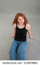 schöne vorbildliche Rothaarige des jungen Mädchens. Modell in Jeans und schwarzem Oberteil auf grauem Hintergrund. Studioaufnahmen. Modell mit roten Haaren und ungewöhnlichem Aussehen.