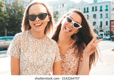 Two young beautiful smiling hipster female in trendy summer dresses.Sexy carefree women posing in the street. Positive pure models having fun at sunset, hugging and going crazy. Show peace sign