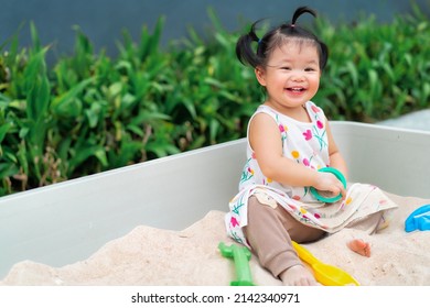 Asian baby laugh and play sand in sandbox at outdoor. 1 year 6 month baby enjoy to play sand use as concept of play, health, mood and motion of baby and kid development.