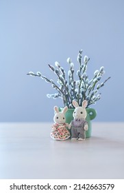 Lindos juguetes de conejito y ramo primaveral de ramas de sauce en jarrón sobre la mesa, fondo borroso suave abstracto. Temporada de primavera festiva
