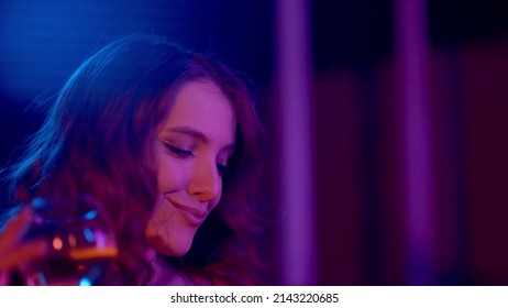 Close-up seorang gadis di klub minum alkohol di bawah lampu neon. Klub malam