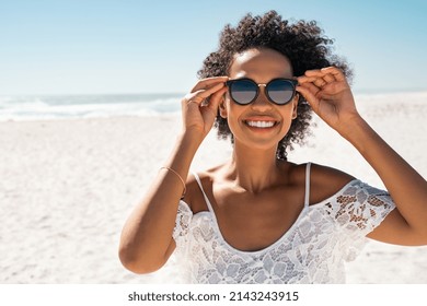 Retrato de una mujer afroamericana sonriente con gafas de sol en la playa con espacio para copiar. Chica negra feliz usando especificaciones de moda mientras sonríe a la orilla del mar. Hermosa mujer relajándose en el mar.
