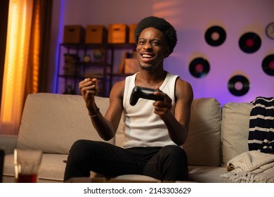 Un atleta maschio vince un round in un gioco per console. L'uomo è seduto sul divano davanti alla TV con il pad in mano, stringendo il pugno per la gioia, sorridendo