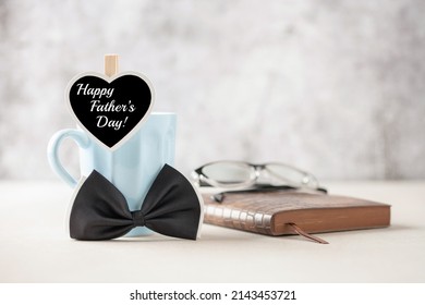 Happy Fathers day concept. Blue coffee cup with black heart and bow tie, notebook and glasses