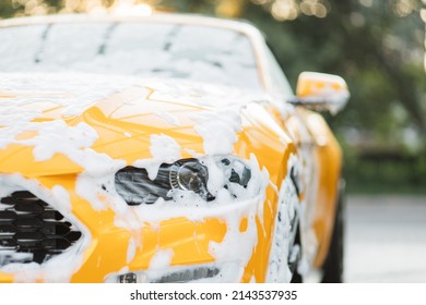 Close-up horizontale opname van gele autokoplamp met reinigingsschuim, gewassen in de wasstraat buiten met hogedrukspuit. Schoon autoconcept. Carwash buiten.