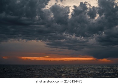 Lindo pôr do sol sobre o mar com nuvens dramáticas cinzentas e faixa laranja do pôr do sol, céu dramático. Foco seletivo nas nuvens