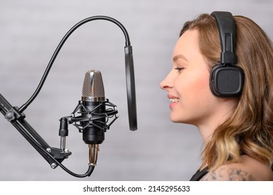 Mädchen singt in ein Mikrofon, mit Kopfhörern in einem Studio. Lieder produzieren und kreieren, Musik machen, einen Track aufnehmen. Ein Album schreiben