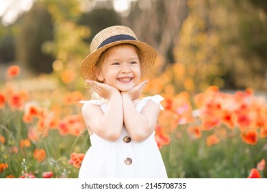 Cute funny baby girl 2-3 year old wear straw hat and white summer dress over flower meadow background. Kid laughing outdoors over nature. Looking at camera. Childhood. 