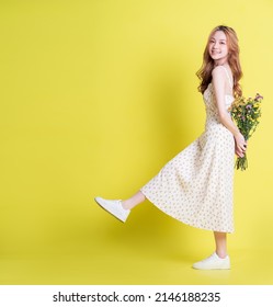 Image of young Asian woman holding flowers on yellow background