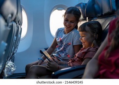 Adorables niñas viajan en avión. Niños lindos se sientan en la ventana de un avión y usan una tableta digital durante el vuelo. Familia viajando al extranjero con niños