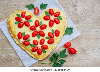 Heart shaped vegetarian Italian pizza with flower shaped tomatoes,cauliflowers and parleys on parchment paper with wooden background.Love concept for Valentine's day and Mother's day.Top view