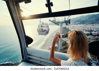 Traveling by Turkey. Young tourist woman sitting in Alanya's cable car enjoying view taking photo on her smartphone.