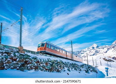 Red train moving towards gornergrat station. View of snow covered landscape against blue sky. Beautiful scenery during winter in alps.