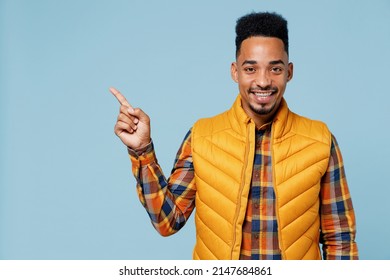 Promoter fun young black man 20s years old wears yellow waistcoat shirt looking camera pointing away on workspace area copy space mock up isolated on plain pastel light blue background studio portrait