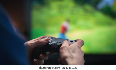 Primer plano de las manos de un hombre en su casa, sentado en un sofá en un elegante apartamento tipo loft y jugando a un videojuego arcade de disparos en una consola. Hombre usando un mando para jugar a un juego multijugador masivo en línea de estilo Battle Royale.