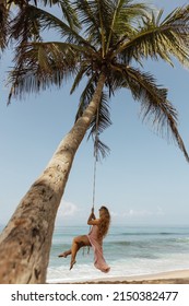 A girl in a dress swings on a bungee in her palm on the beach of Sri Lanka