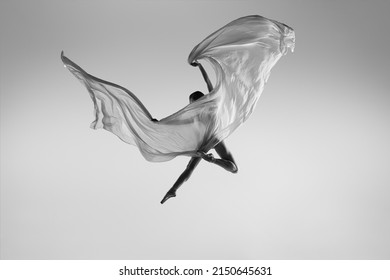 Like butterfly. Black and white portrait of graceful ballerina dancing with fabric, cloth isolated on grey studio background. Grace, art, beauty, contemp dance concept. Weightless, flexible actress