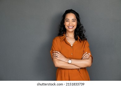 Retrato de una joven latina con una sonrisa agradable y brazos cruzados aislada en una pared gris con espacio para copiar. Hermosa chica con los brazos cruzados mirando a la cámara contra la pared gris. Mujer hispana alegre