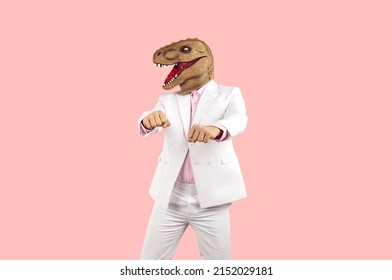 Un tipo raro con un disfraz divertido bailando con un fondo de estudio rosa pastel. Un hombre excéntrico alegre con traje blanco y una máscara de dinosaurio mascarada loca y fea tonta divirtiéndose en una fiesta loca