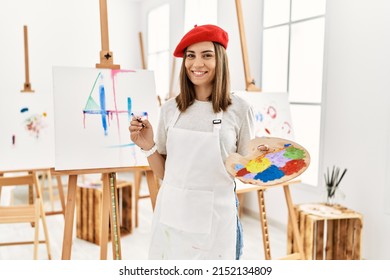 Mujer joven artista pintando en un lienzo en el estudio de arte con una sonrisa feliz y fresca en la cara. persona con suerte.
