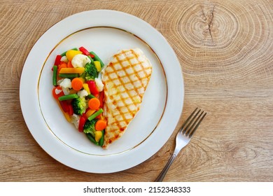 Heart shape grilled chicken breast with steamed vegetables on plate with wooden table background.Love healthy food concept for Valentine's day and Mother's day.Top view.Copy space