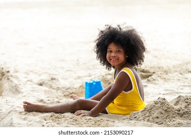 熱帯のビーチに座って、夏休みに笑顔で砂やビーチのおもちゃを遊んでいる小さなかわいいアフリカの子供の女の子。幸せな子供の子供は、ビーチでの休暇旅行で野外活動のライフスタイルを楽しんで楽しんでいます