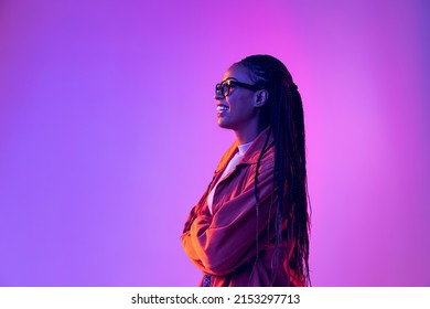 Profielmening van jong meisje met afrokapsel in katoenen overhemd dat op paarse achtergrond in neonlicht wordt geïsoleerd. Concept van schoonheid, kunst, mode, jeugd, verkoop en advertenties. Mooie vrouw die lacht