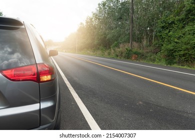 Автомобіль, що працює на асфальтованій дорозі для поїздки по прямій вигнутій дорозі вперед. З зеленим лісом біля дороги. Задній ліхтар автомобіля ввімкніть світло signl. Біла лінія та суцільна жовта лінія на дорозі.