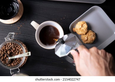 Tampilan atas, Barista menuangkan kopi dari pembuat kopi moka pot ke cangkir kopi. Tangan memegang pot moka klasik Italia menuangkan kopi.