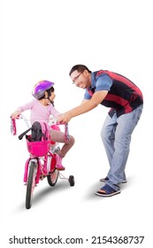 Portrait of young father teaching his daughter to riding a bicycle in the studio. Isolated on white background
