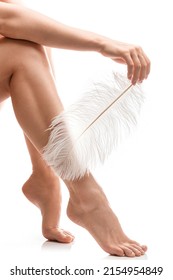 Primer plano de pies femeninos con piel suave y suave pluma de avestruz sobre fondo blanco.