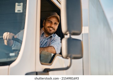 Gelukkige professionele vrachtwagenchauffeur die zijn vrachtwagen bestuurt en naar de camera kijkt. Ruimte kopiëren.