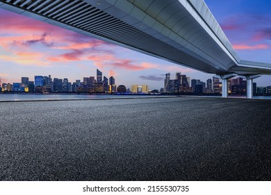 Carretera asfaltada vacía y horizonte urbano moderno con edificios en Hangzhou al atardecer, China.
