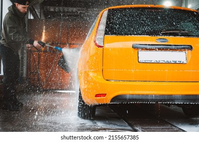 Een gele auto wassen bij een contactloze self-carwash. Een sedan-auto wassen met schuim en water onder hoge druk. Voorjaarsschoonmaak bij de wasstraat.