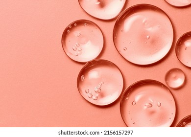Öltropfen auf lachsrosa Rosenfarbhintergrund. Klares flüssiges Kosmetikproduktmakro. Serum-Gel-Textur mit Blasen in der Nähe