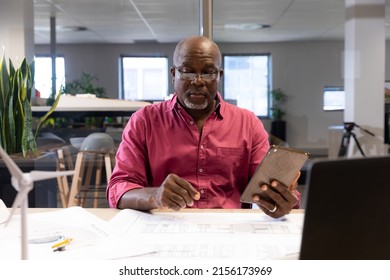 机の上の青写真を分析しながらデジタル タブレットを保持している成熟したアフリカ系アメリカ人のエンジニア。変更されていない、創造的なビジネス、テクノロジー、モダンなオフィスのコンセプト。