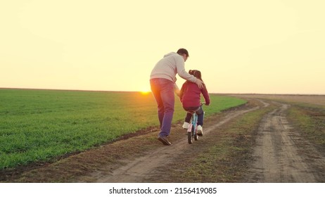Father teaches little kid girl to ride child's bike on road, in fall, in spring. Happy family, dad teaches his daughter, child to ride bike in park at sunset. Happy family, childhood. Parent, child
