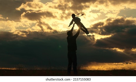 お父さんは娘と遊び、手で子供を空に投げ上げ、幸せな子供です。娘の父は、太陽と雲を背景に公園で一緒に遊びます。屋外で幸せな家族のシルエット。