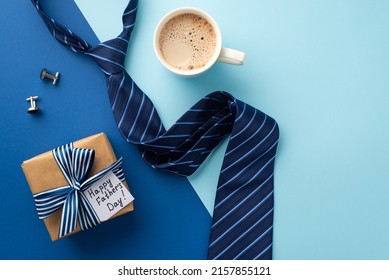 Vatertagskonzept. Draufsichtfoto einer Geschenkbox aus Bastelpapier mit Schleife aus Seidenband und blauer Krawatte, Tasse Kaffee und Manschettenknöpfen auf zweifarbigem blauem Hintergrund