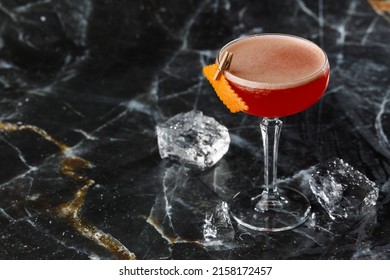 Koktail asam merah dalam gelas coupe dihiasi dengan kulit jeruk. Klub semanggi dengan gin impor. Pada latar belakang marmer hitam.