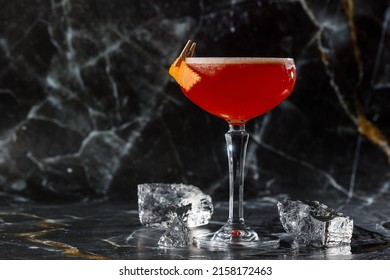 Koktail asam merah dalam gelas coupe dihiasi dengan kulit jeruk. Klub semanggi dengan gin impor. Pada latar belakang marmer hitam.
