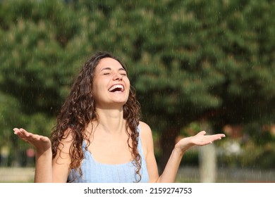 Mujer feliz riendo y disfrutando bajo una lluvia repentina en un día soleado