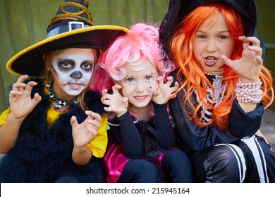 Portrait of three little girls in Halloween costumes looking at camera with frightening gesture
