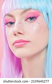 Maquillaje de anime. Chica guapa con maquillaje brillante, pecas brillantes y peluca de color violeta-azul sobre un fondo rosa. Peinado, coloración del cabello, maquillaje. Estilo anime japonés.
