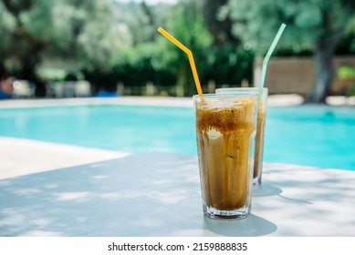 
Summer holiday vacation with frappe refreshment by luxury poolside. Two ice coffee cups with straws behind resort summer pool bar. Greek fredo cappuccino cold drink at beach hotel. 