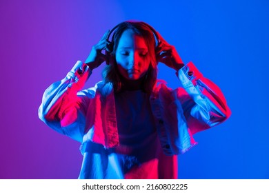 Hipster igen teenager beautiful fashion girl model wear stylish  headphones enjoy listening to new cool music mix stand on purple studio background in trendy 80s 90s club blue party light. 