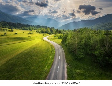 夏の日没時の緑の牧草地の道路の空撮。田舎道、山、森のドローンからの平面図。車道、太陽の光、木、丘、緑の草、雲のある美しい風景。スロベニア