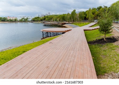 Un camino de madera a lo largo del terraplén del lago, la construcción de un parque de la ciudad en un estanque, una plataforma de tablas, diseño de paisaje moderno, paisajismo de la ciudad, un lugar para relajarse junto al agua