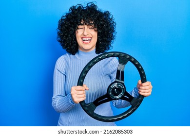 Young middle east woman holding steering wheel smiling and laughing hard out loud because funny crazy joke. 